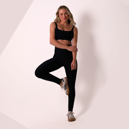 Woman wearing black athletic wear posing on a white background